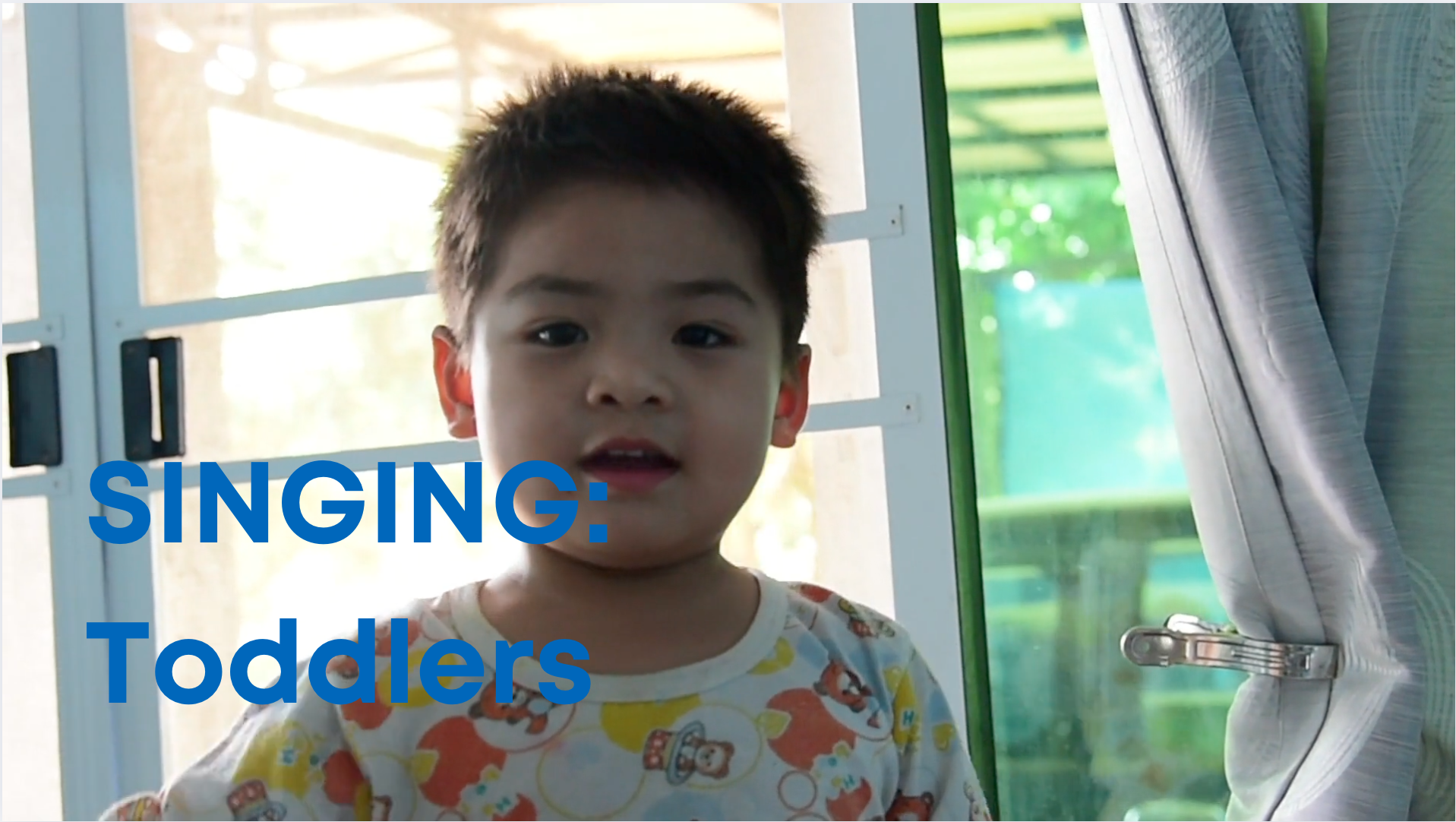 A toddlers stands on a bed smiling and singing